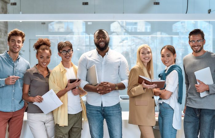 Portrait of young and successful co-workers in casual wear smiling at camera while standing in working space. Teamwork concept. Collaboration